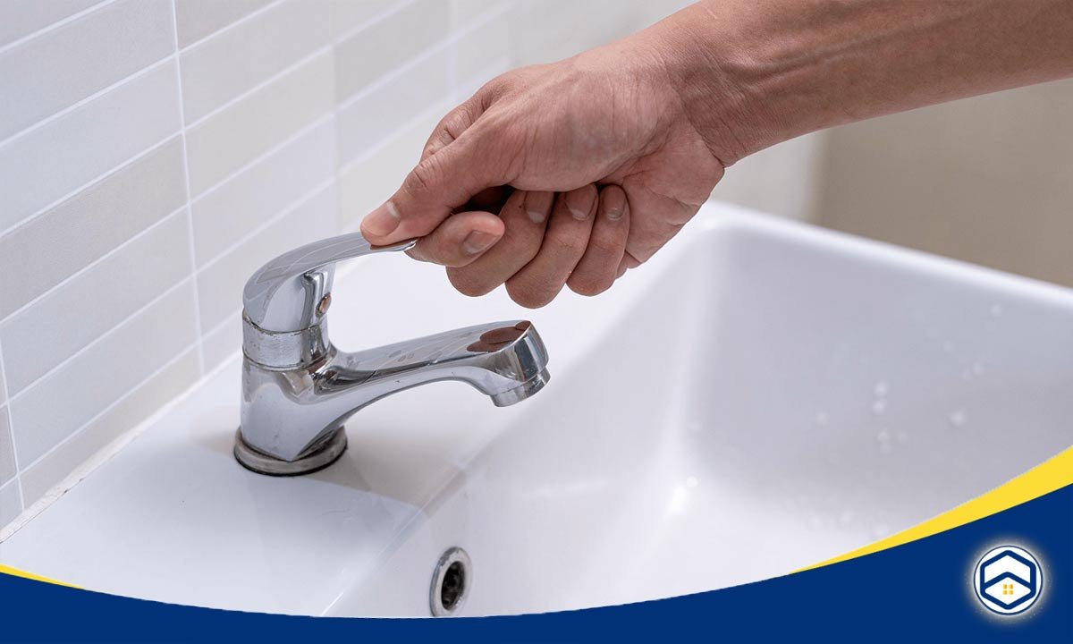 A person is turning on a chrome faucet in a bathroom sink, preparing to use water.