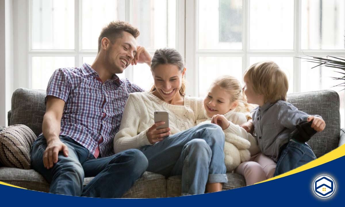 A joyful family sits together on a couch, sharing a moment while looking at a smartphone.