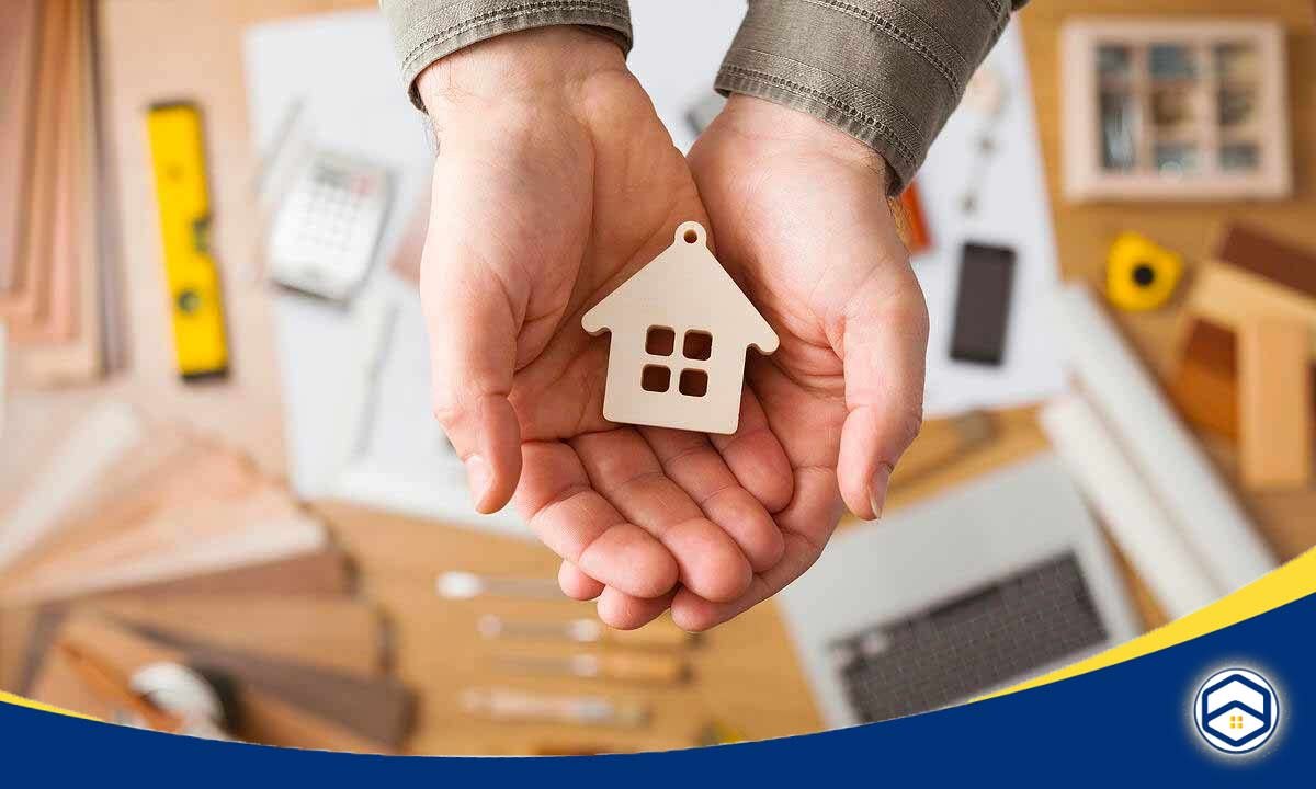 A person holds a wooden house-shaped keychain in their open hands, surrounded by various tools