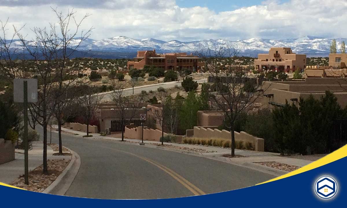 The image appears to show a scenic view of Santa Fe, New Mexico, with adobe-style buildings, mountains in the background, and a winding road in the foreground. 