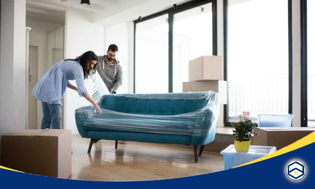 The image shows a couple working together to move and set up a new sofa or couch in their apartment, which highlights one of the pros of living in an apartment