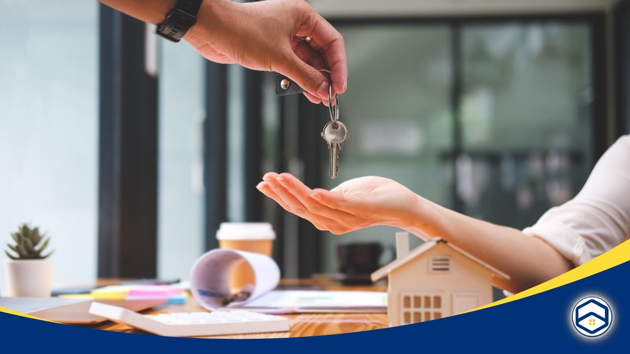 A hand passing house keys to another over a desk with papers and a miniature house, symbolizing rental agreement success.