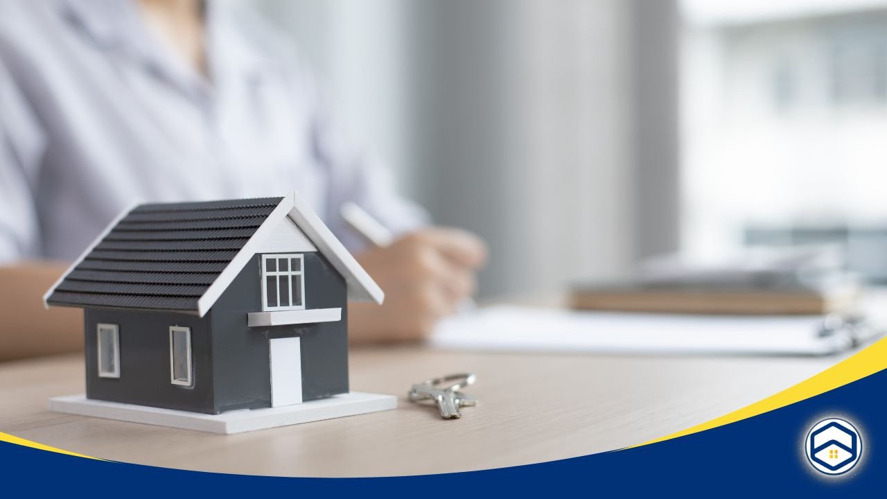 Miniature house model with keys on a table, and a person signing paperwork in the background.