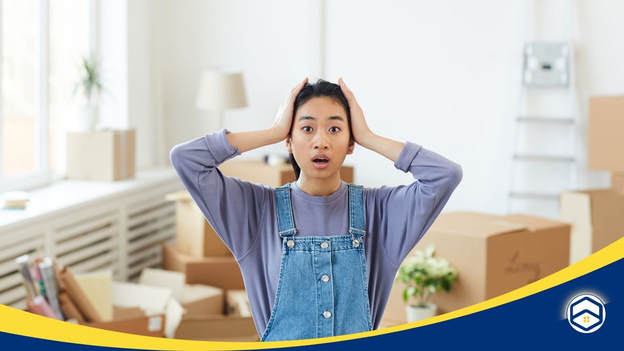 Surprised woman in overalls surrounded by moving boxes in a bright room.