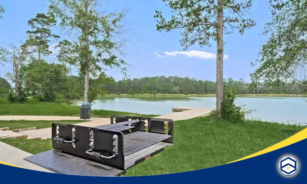 The image shows a scenic lakeside setting in the Deer Pines neighborhood of Conroe, Texas, with a wooden dock and benches overlooking the peaceful waters.