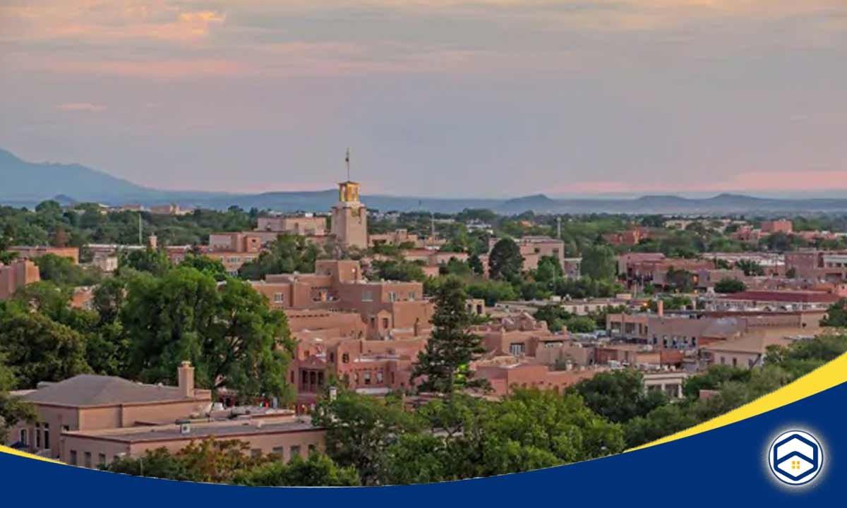 The image appears to show a panoramic view of the Eldorado at Santa Fe community, showcasing the distinctive adobe-style architecture, lush greenery, and scenic mountain