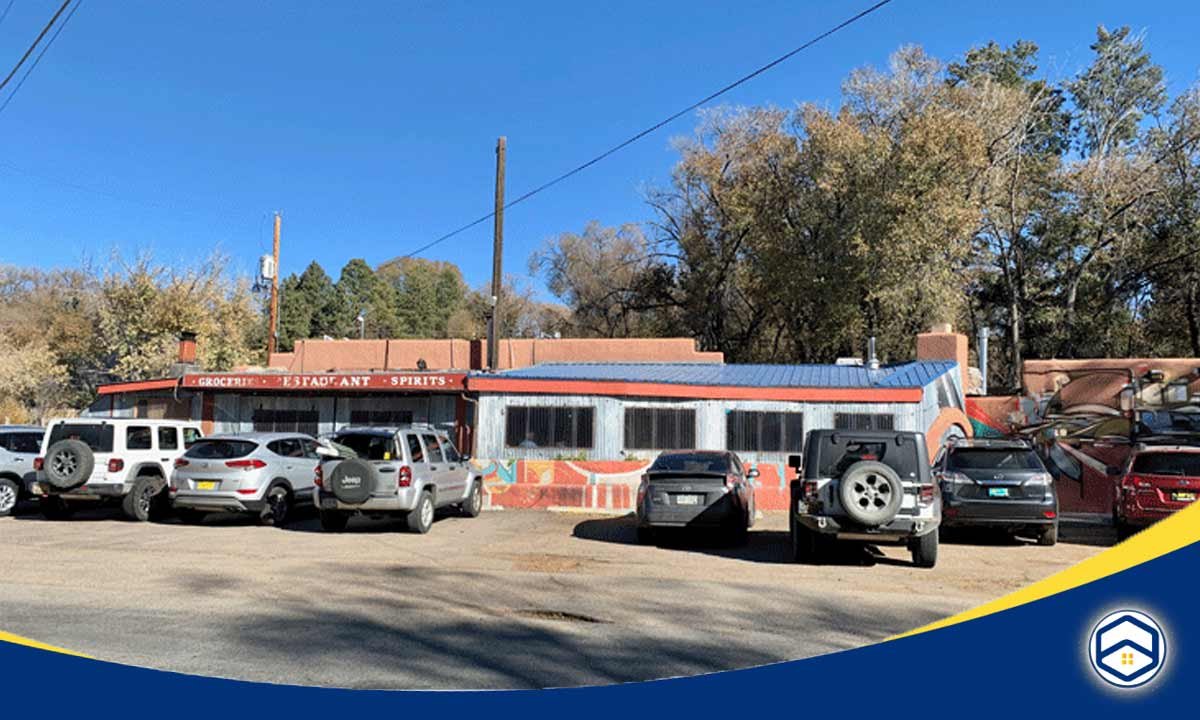 The image captures a cluster of buildings, including a restaurant and spirits shop, surrounded by vehicles parked in the lot, suggesting a lively commercial district in this top-rated Santa Fe community.