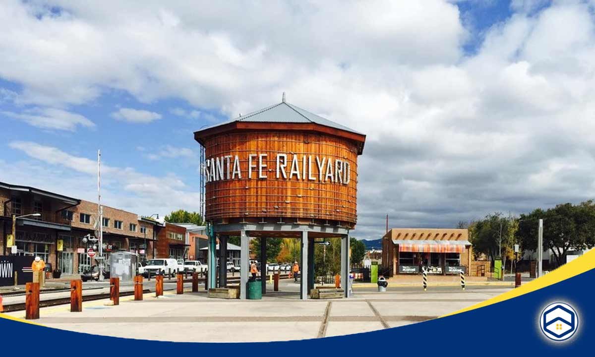 The image shows the historic Santa Fe Railyard District, a top-rated community within Santa Fe, New Mexico, featuring a distinctive wooden water tower with the "Santa Fe Railyard" signage.