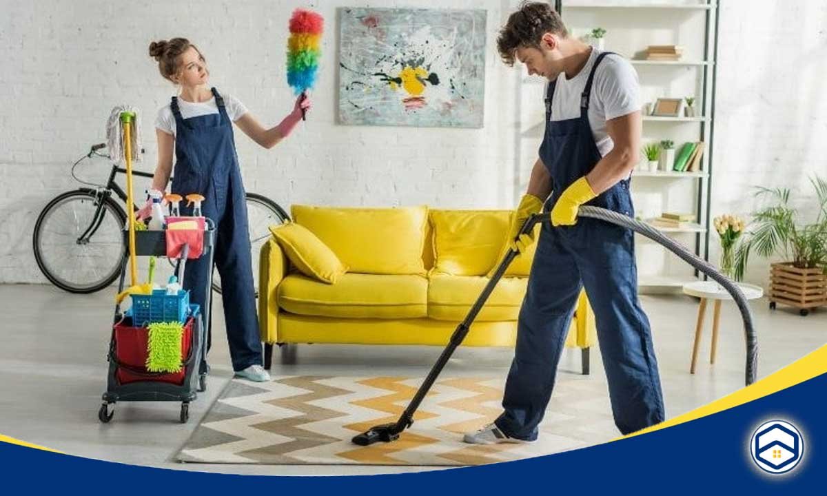 The image shows two cleaning workers, one using a vacuum cleaner and the other holding a cleaning tool, working together to clean a living room with a yellow sofa.