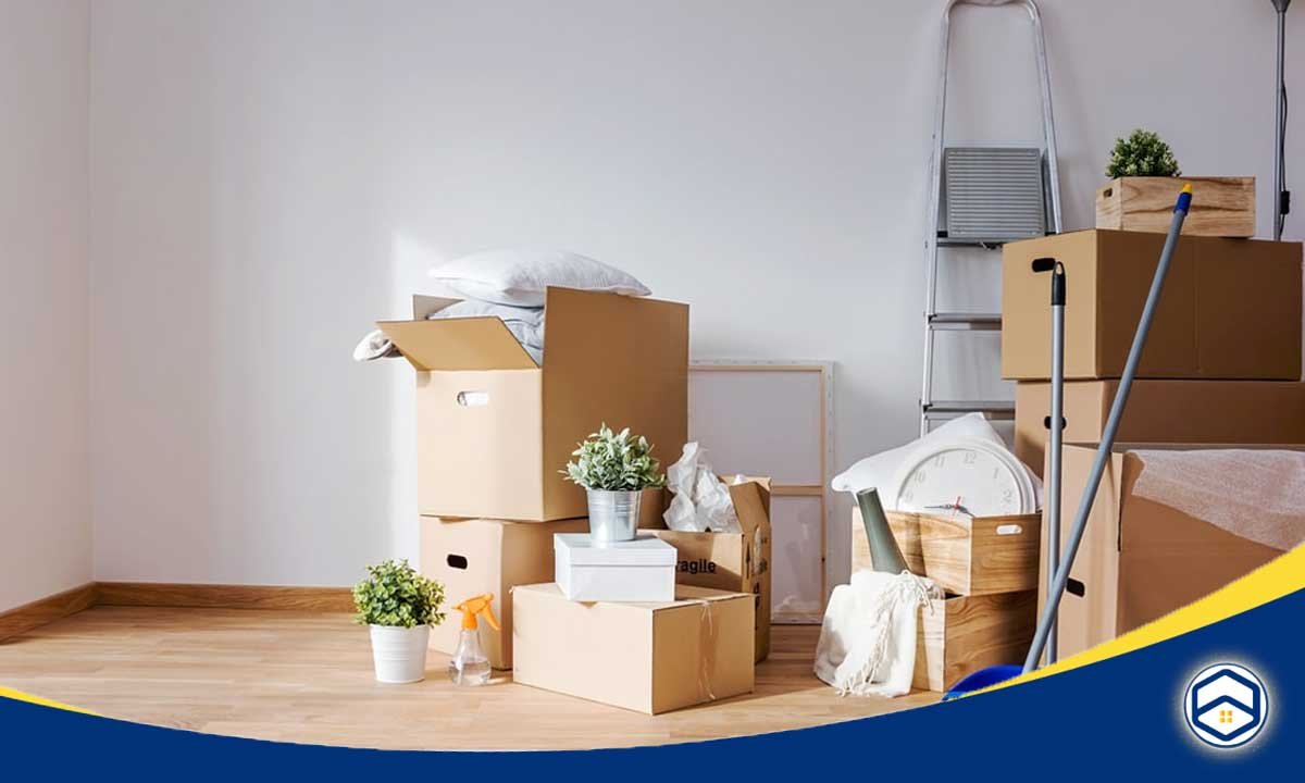 The image shows a cluttered room with various moving boxes, furniture, and household items, indicating a move-out cleaning scenario for a Houston apartment.